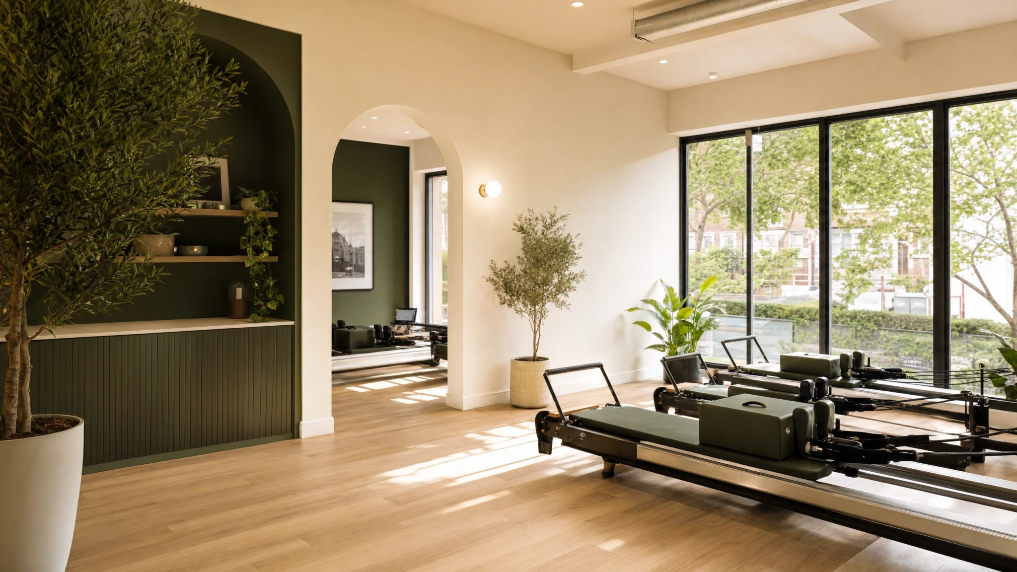 Bright modern Pilates reformer studio with large windows, green accents, and indoor plants.