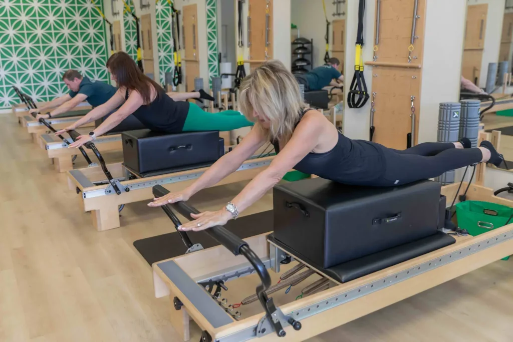 Three people performing back extensions on long boxes during a group Pilates reformer class.