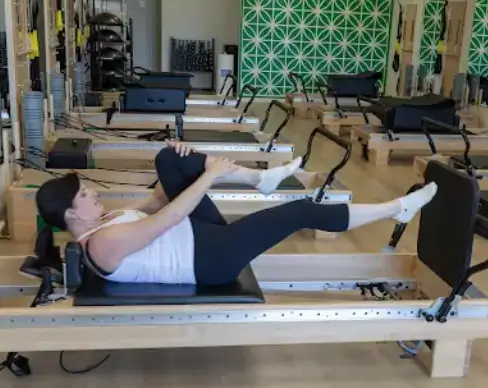 Woman performing a single leg stretch on a Pilates reformer in a modern studio.