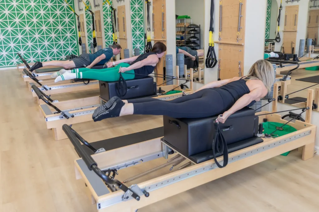 Three people lying on long boxes during a group Pilates reformer class at CharisPilates.