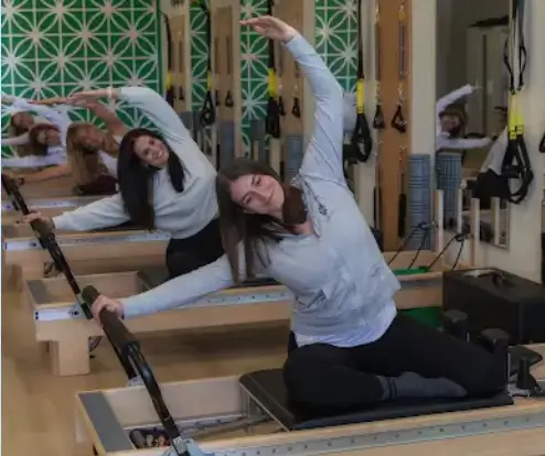 Women performing a seated side stretch on Pilates reformers during a group class.