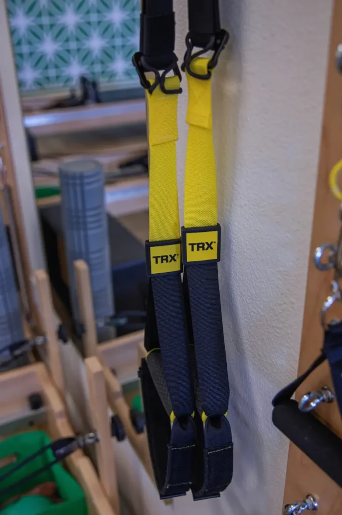Yellow and black TRX suspension training straps hanging in a modern Pilates studio.